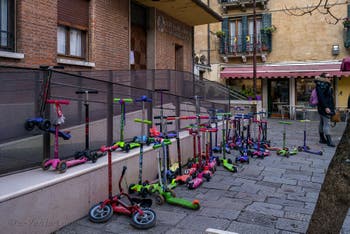 Scène de la vie vénitienne : Troupeau de 41 trottinettes et un vélo attendant les enfants devant une école maternelle à Venise.